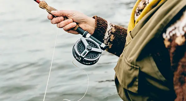 closeup of a person holding fish rod with wheel